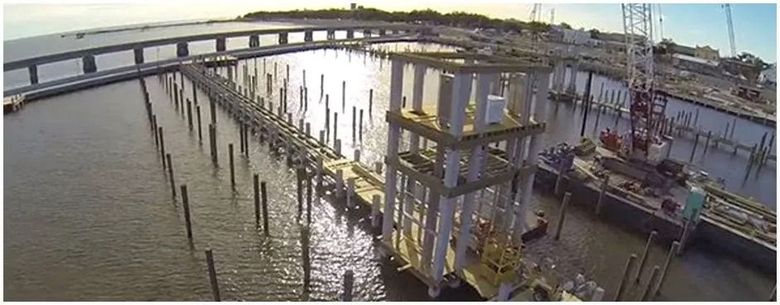 Construction site in a harbor, with a bridge in the background and a crane on the right.