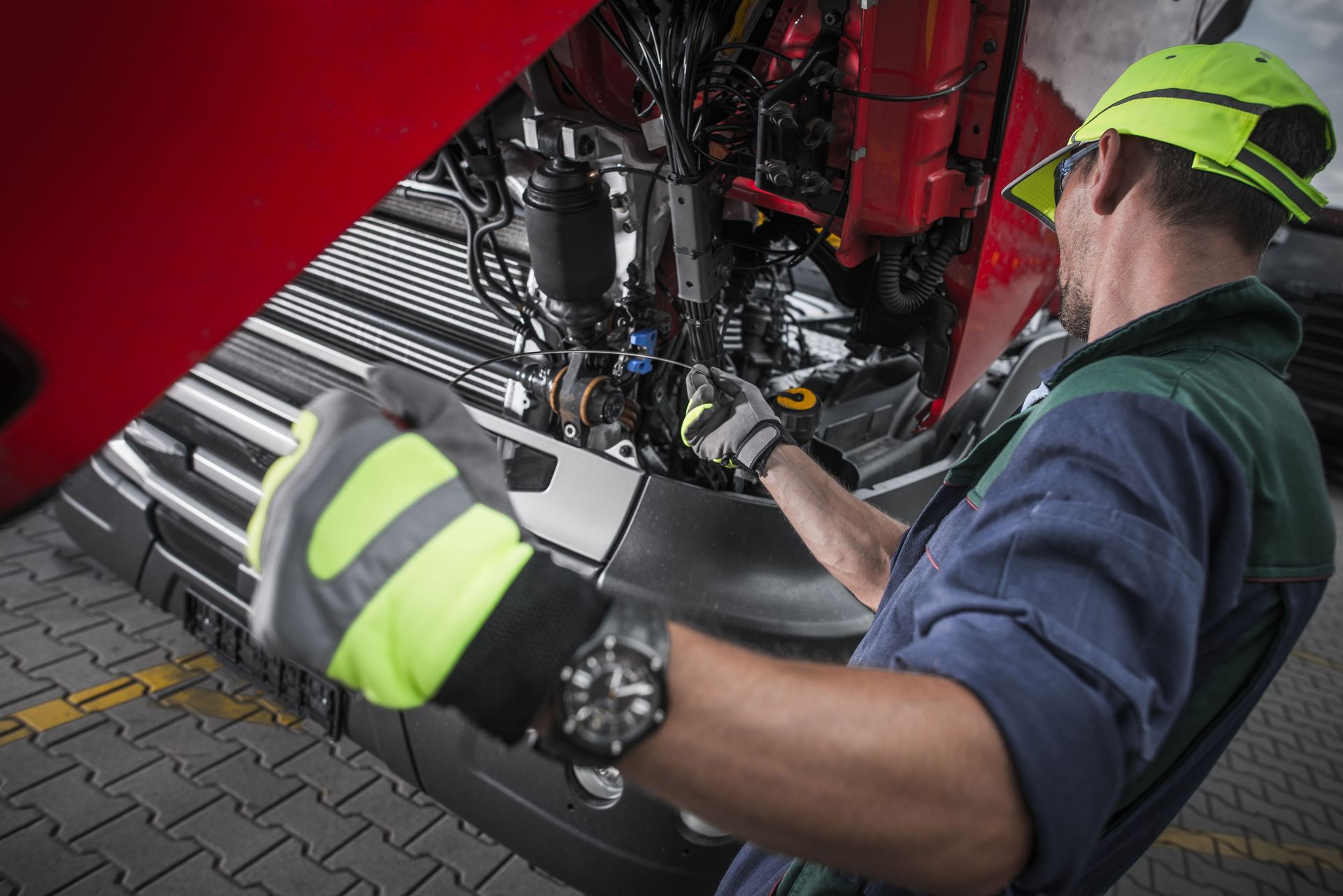 Technician in neon safety gear inspects machinery under a red vehicle