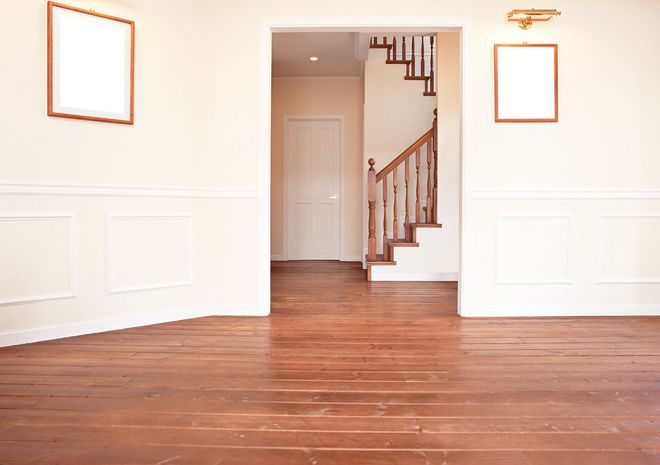 Empty white room with hardwood floor, doorway to a hall with stairs, and two framed wall openings