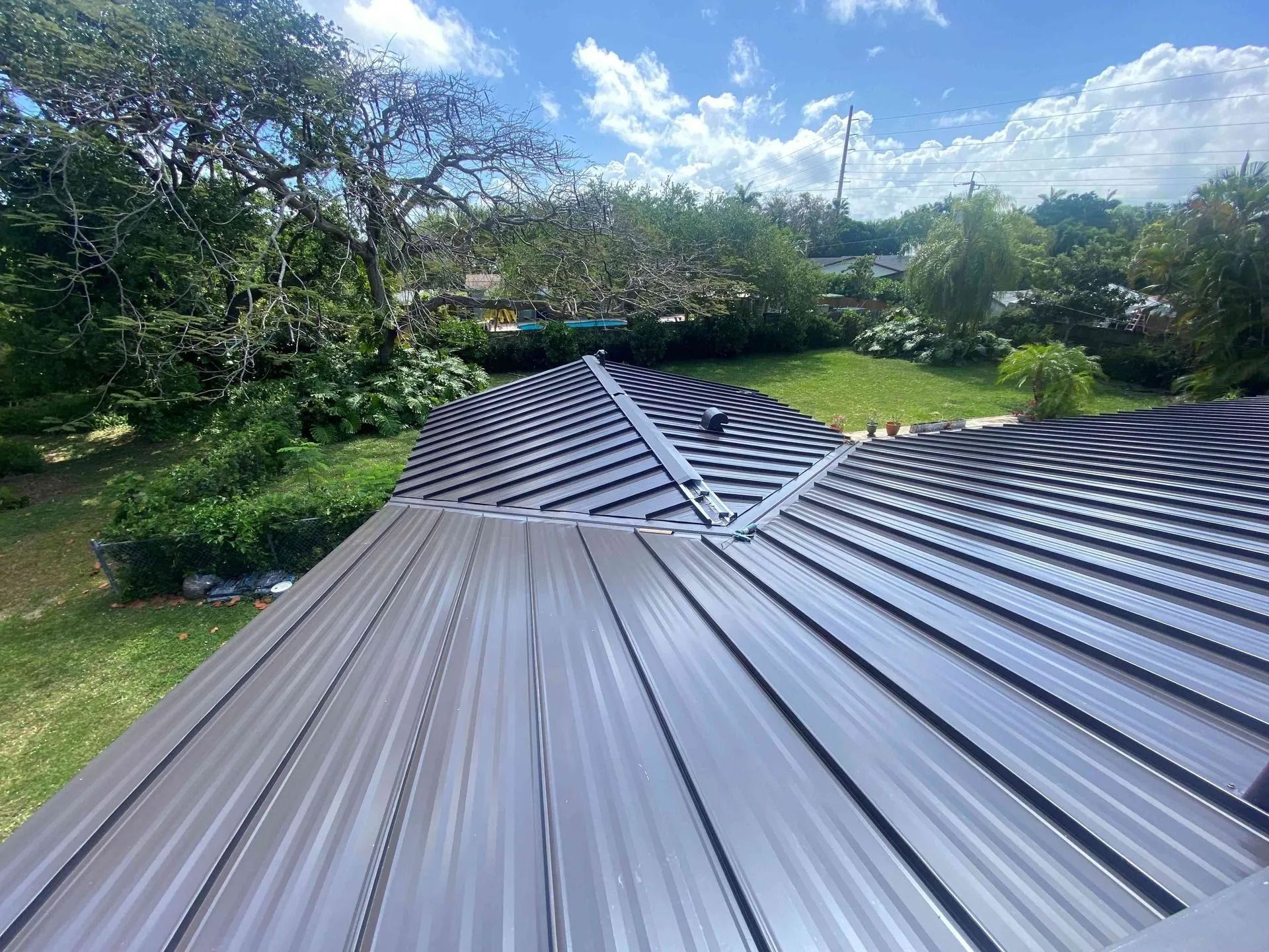 Dark gray metal roof panels with a leafy green garden and blue sky in the background