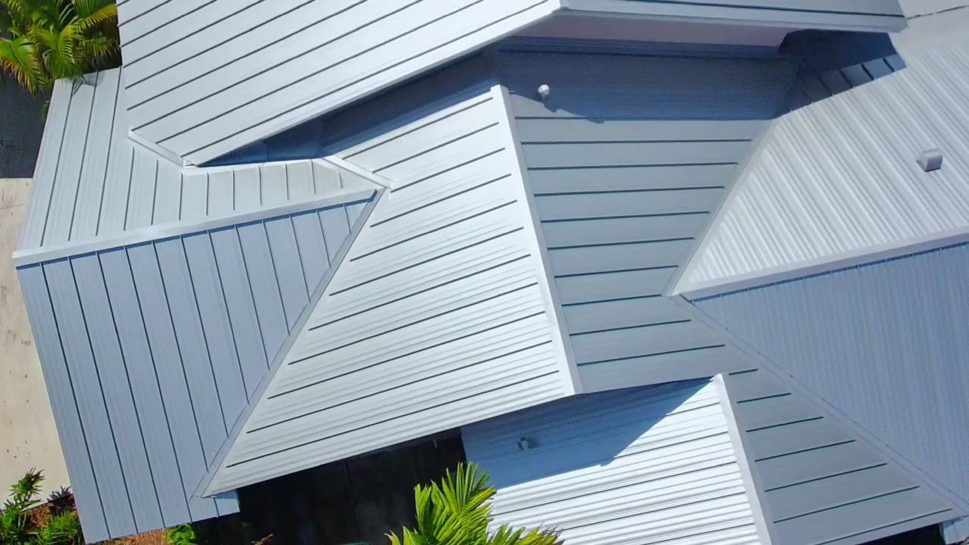 Light gray metal rooftops with intersecting sloped panels and skylights viewed from above