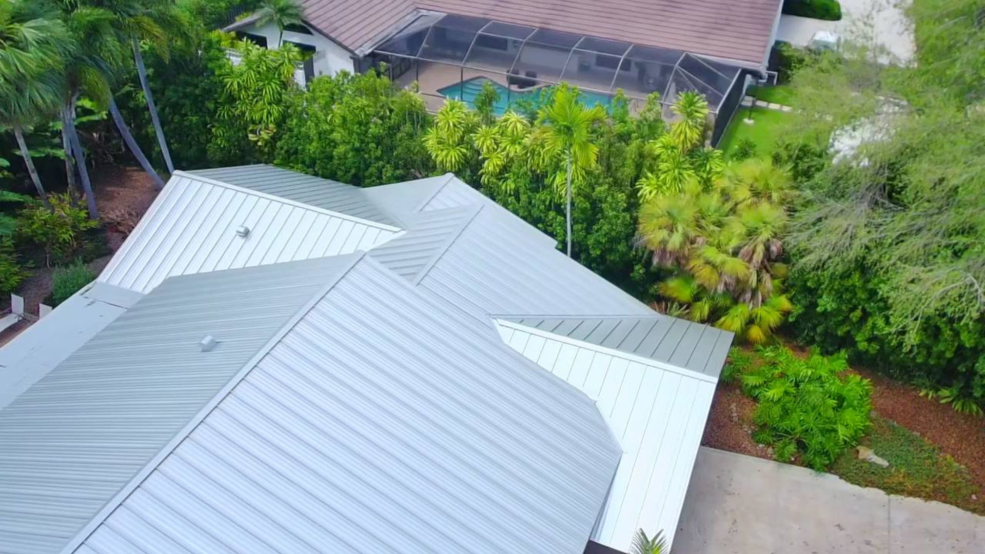 Overhead view of gray metal roofs surrounded by lush green trees and shrubs