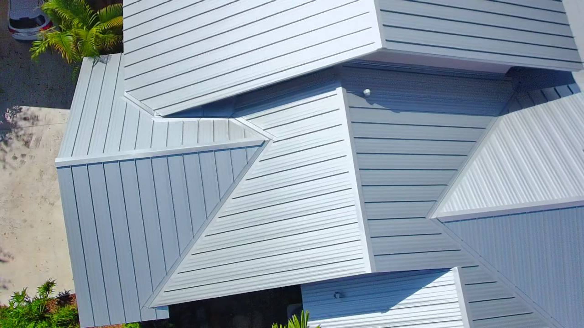 Close-up of a light gray metal roof with intersecting ridges and vents, seen from above.