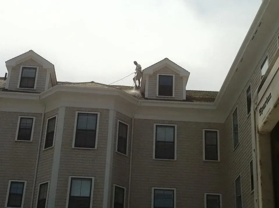 Person pressure washing a roof of a multi-story building on a sunny day.