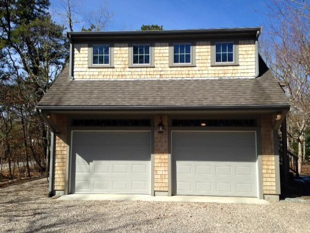 Two-car garage with gray doors, tan cedar shingles, and three small windows above.