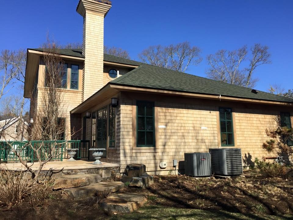 Two-story home with a cedar shingle exterior, green roof, and a brick chimney, under a clear blue sky.