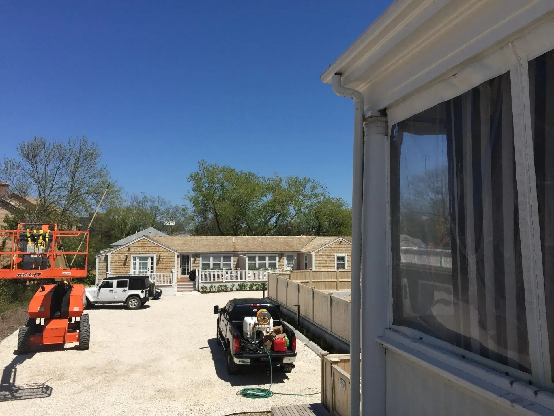 Construction site: trucks, lift, workers, and a building on a gravel lot under a blue sky.