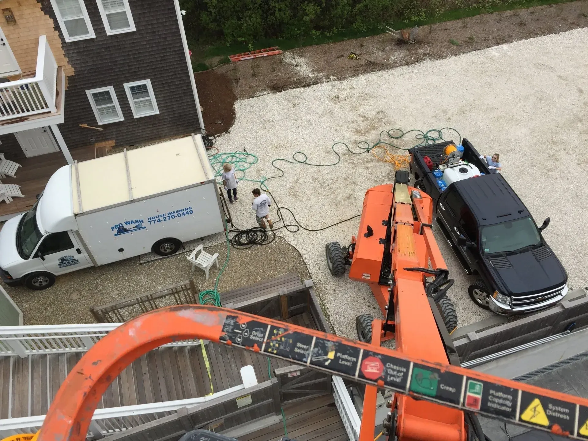 Workers near a white van and black truck on a gravel driveway, with an orange lift in the foreground.