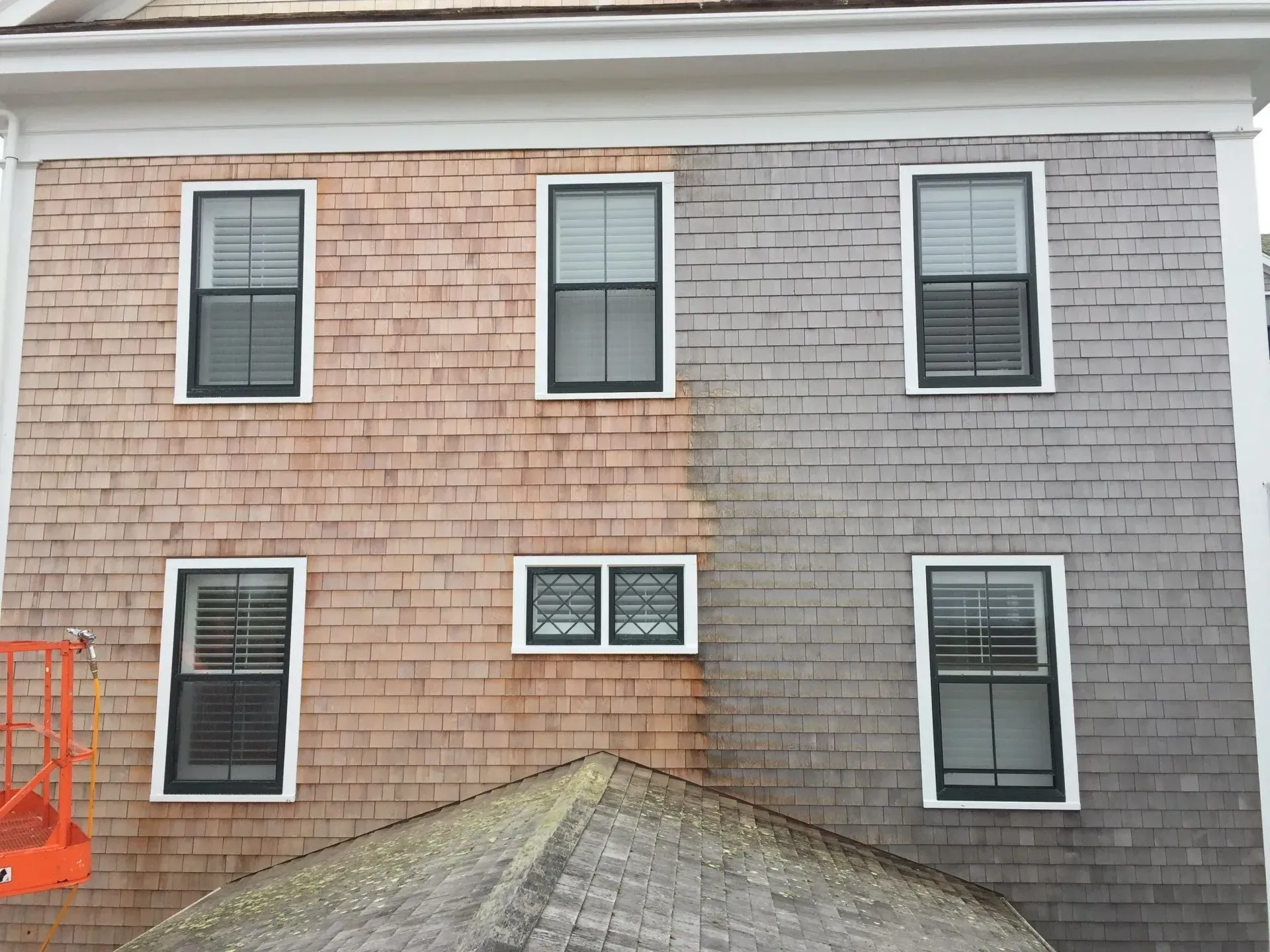 House siding, half stained brown, half gray, with black-framed windows; a lift on the left.