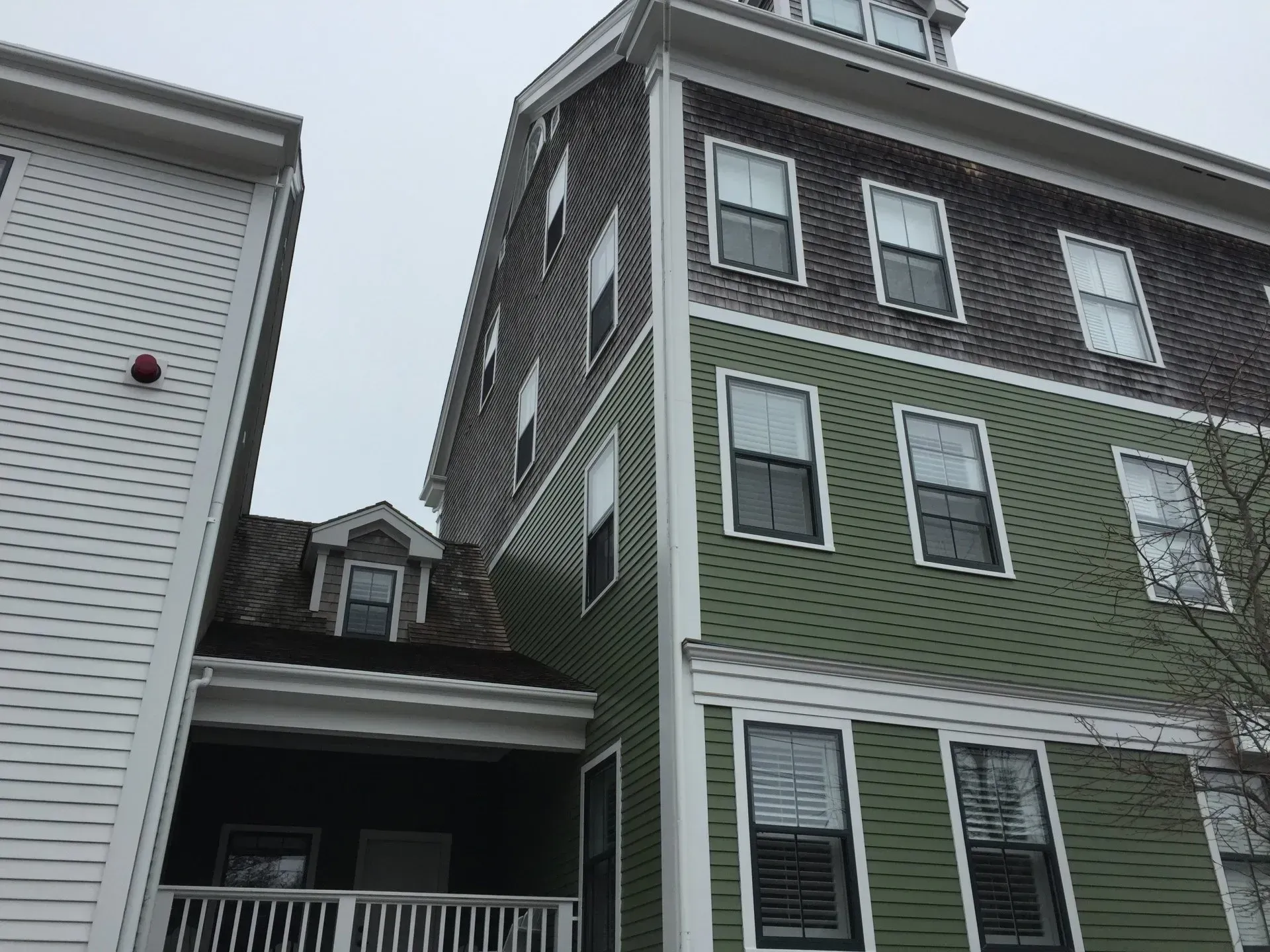 Multi-story building with green and gray siding, windows, and a dormer.