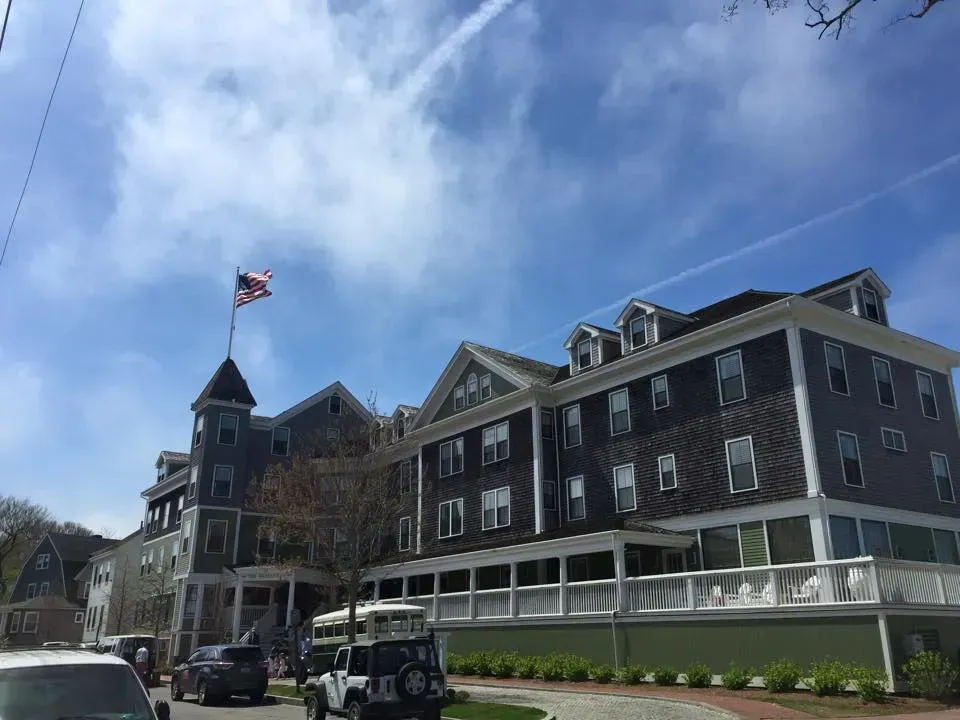 Large gray building with an American flag; blue sky. Cars and a white jeep parked on street.