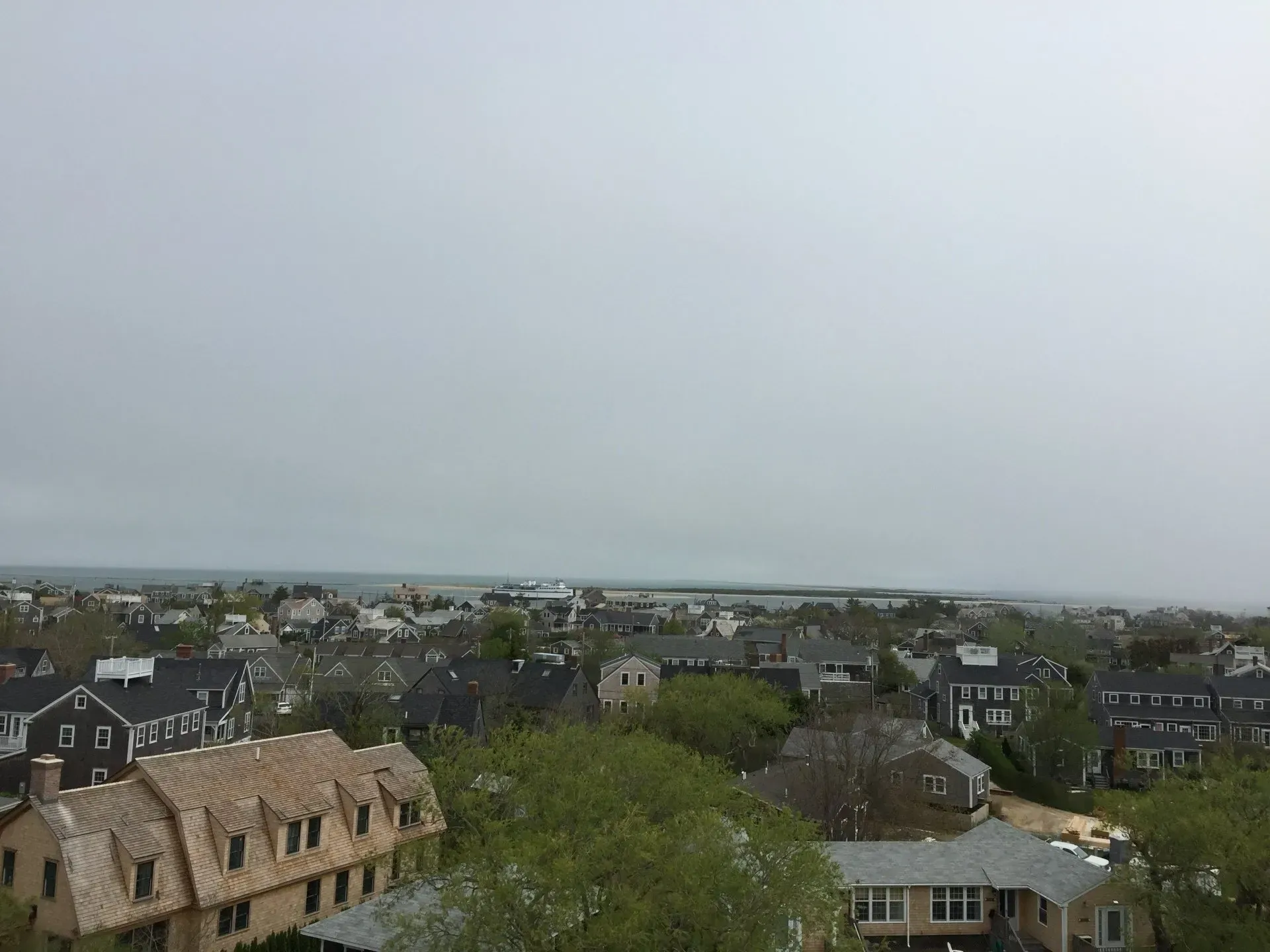View of a town under a gray sky, with houses, trees, and distant water.