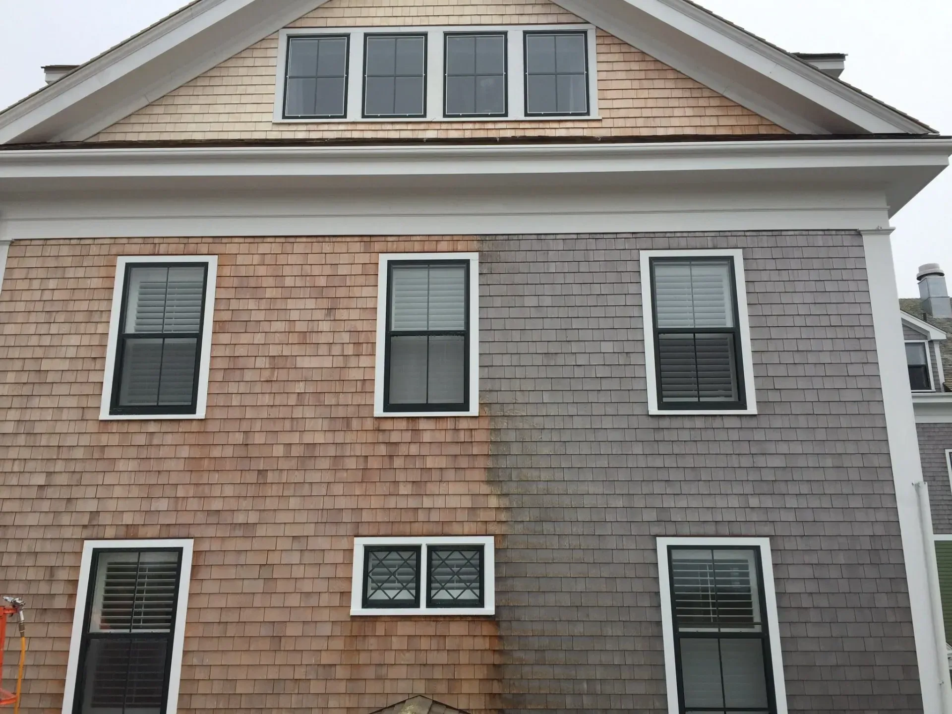 Half of a house's cedar shingle siding is cleaned, showing the contrast between the stained and weathered sections.