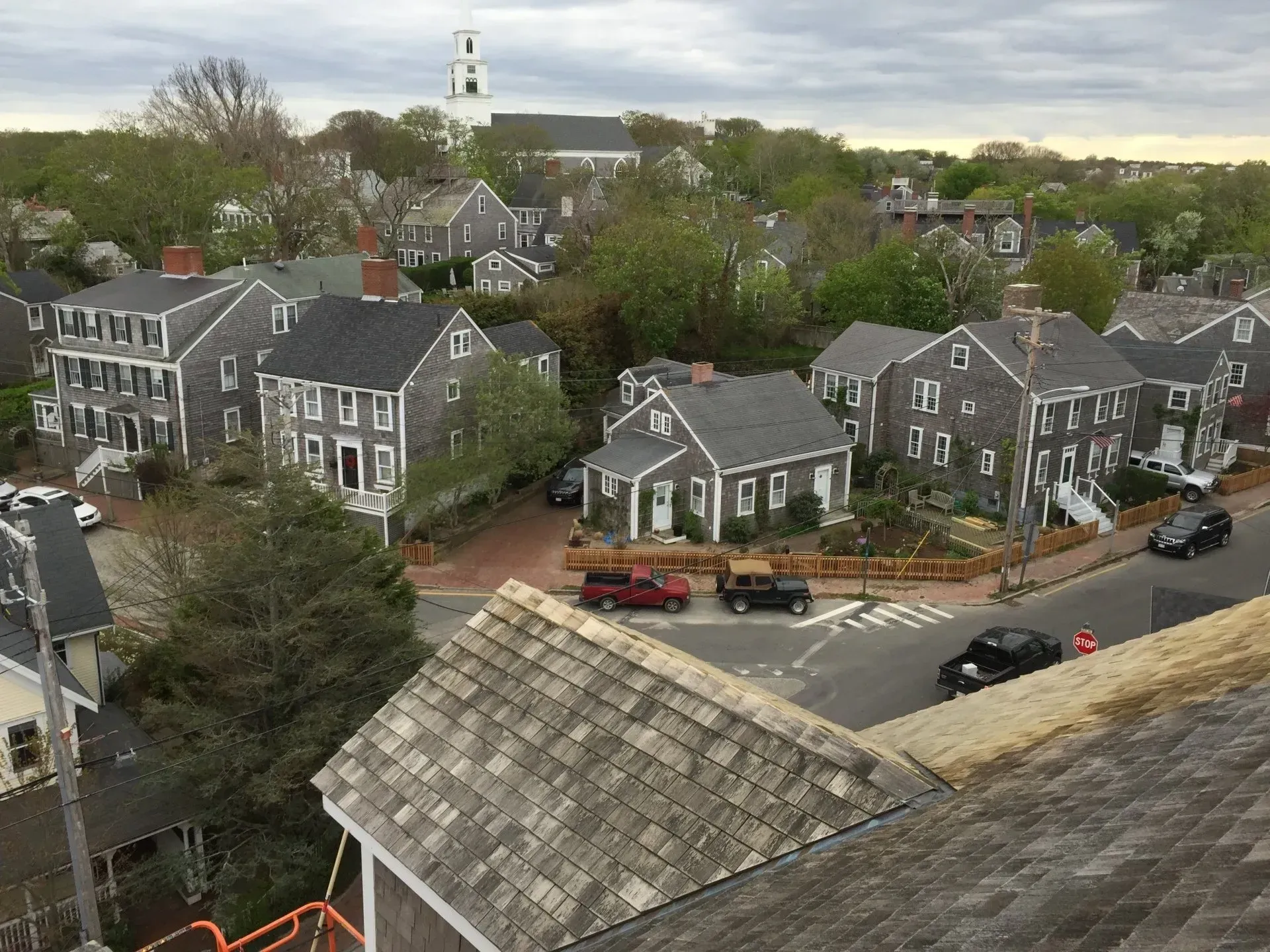 Overhead view of Nantucket town with gray shingle houses, a church steeple, and vehicles on the street.