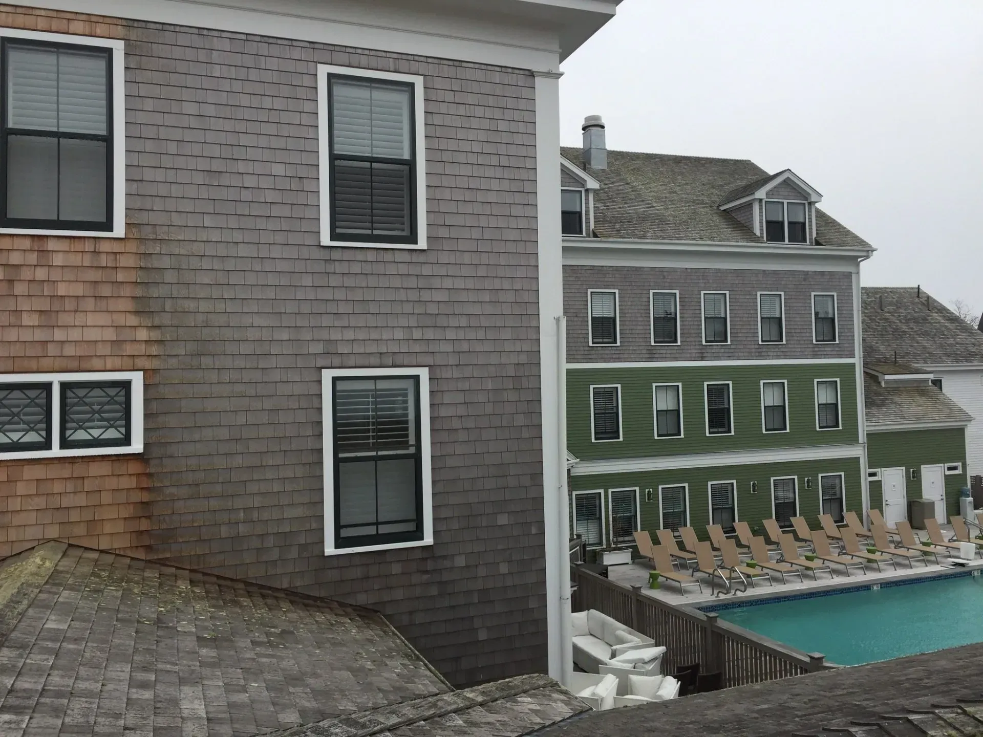 Buildings with grey, brown, and green siding, a swimming pool, and lounge chairs.