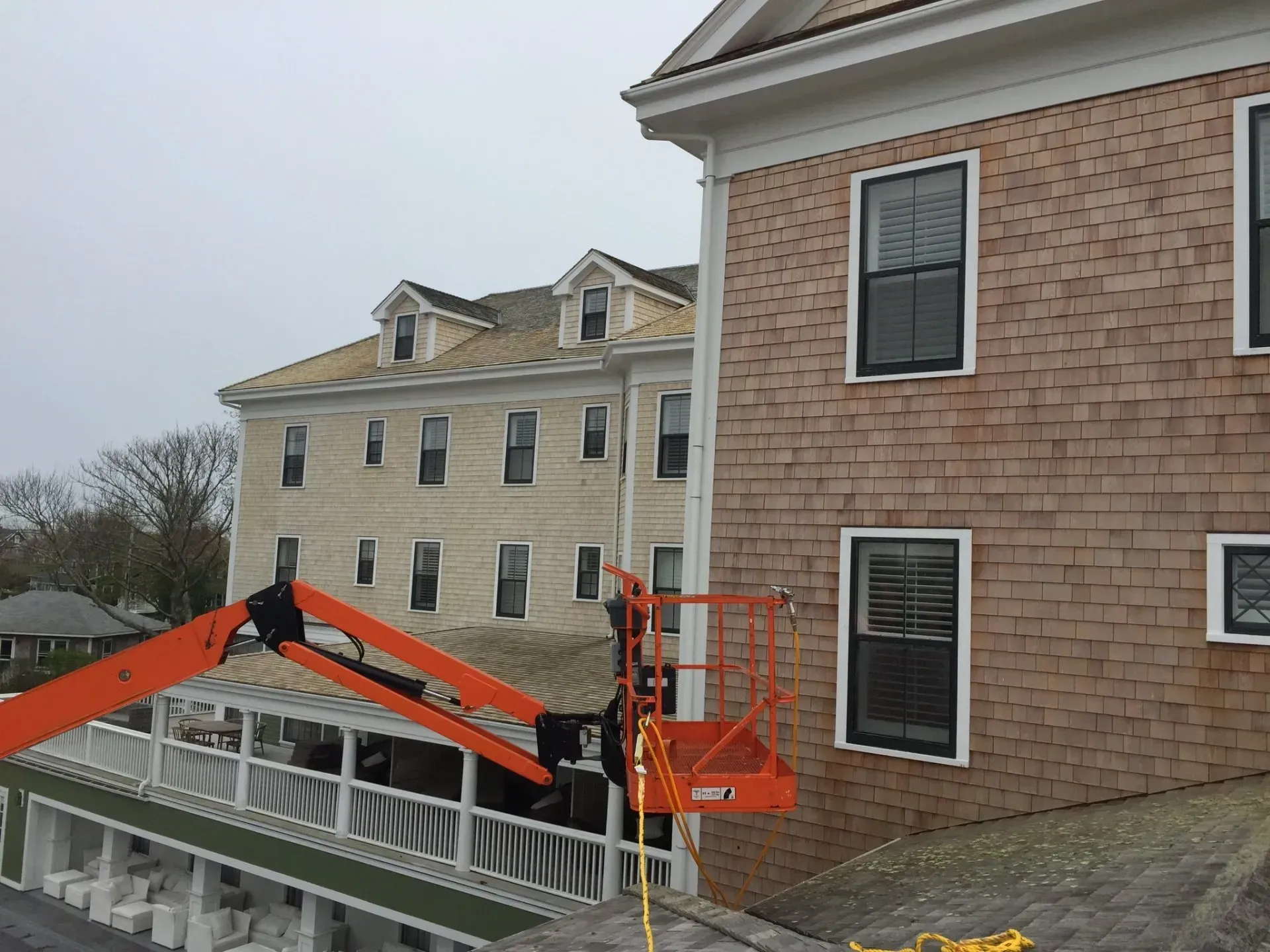 An orange lift reaching towards a building. Tan shingled building with black windows and a light tan building in the background.