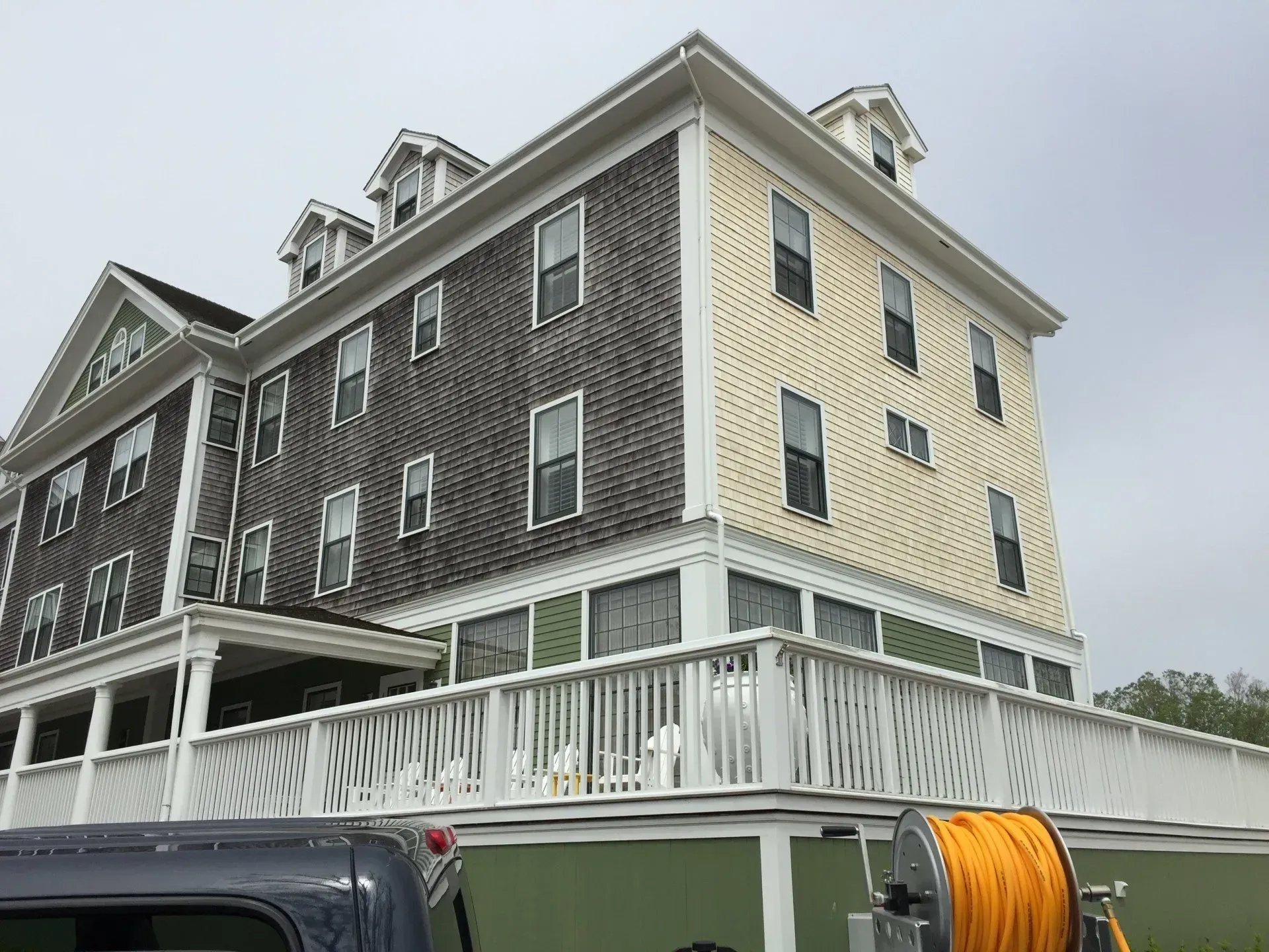 Multi-story building with yellow and gray siding, white trim, and a wrap-around porch.