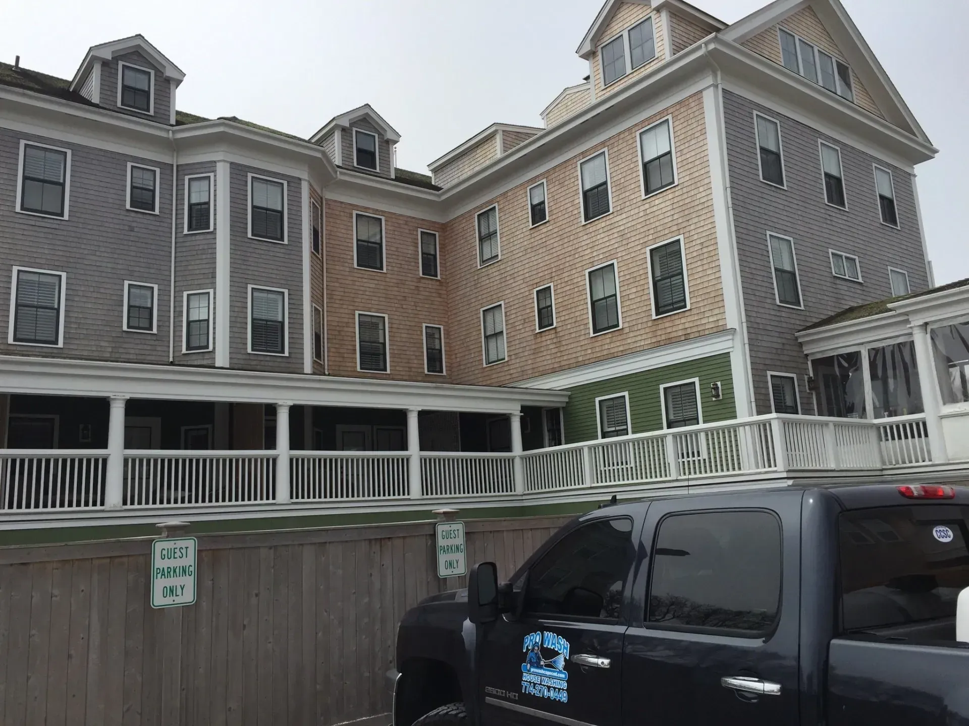 A multi-story building with gray and tan siding. A pickup truck is in front. Cloudy sky.