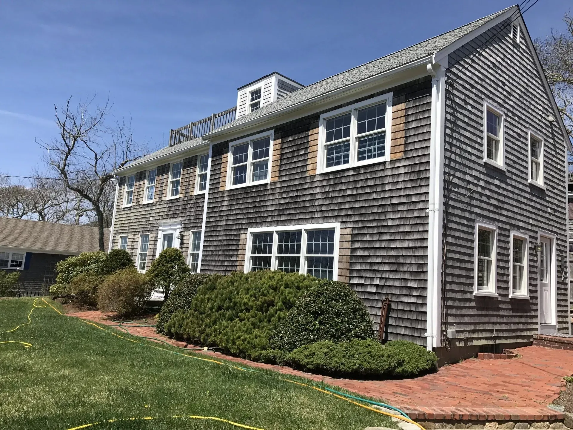 Two-story gray shingled house with white trim, green lawn, blue sky.