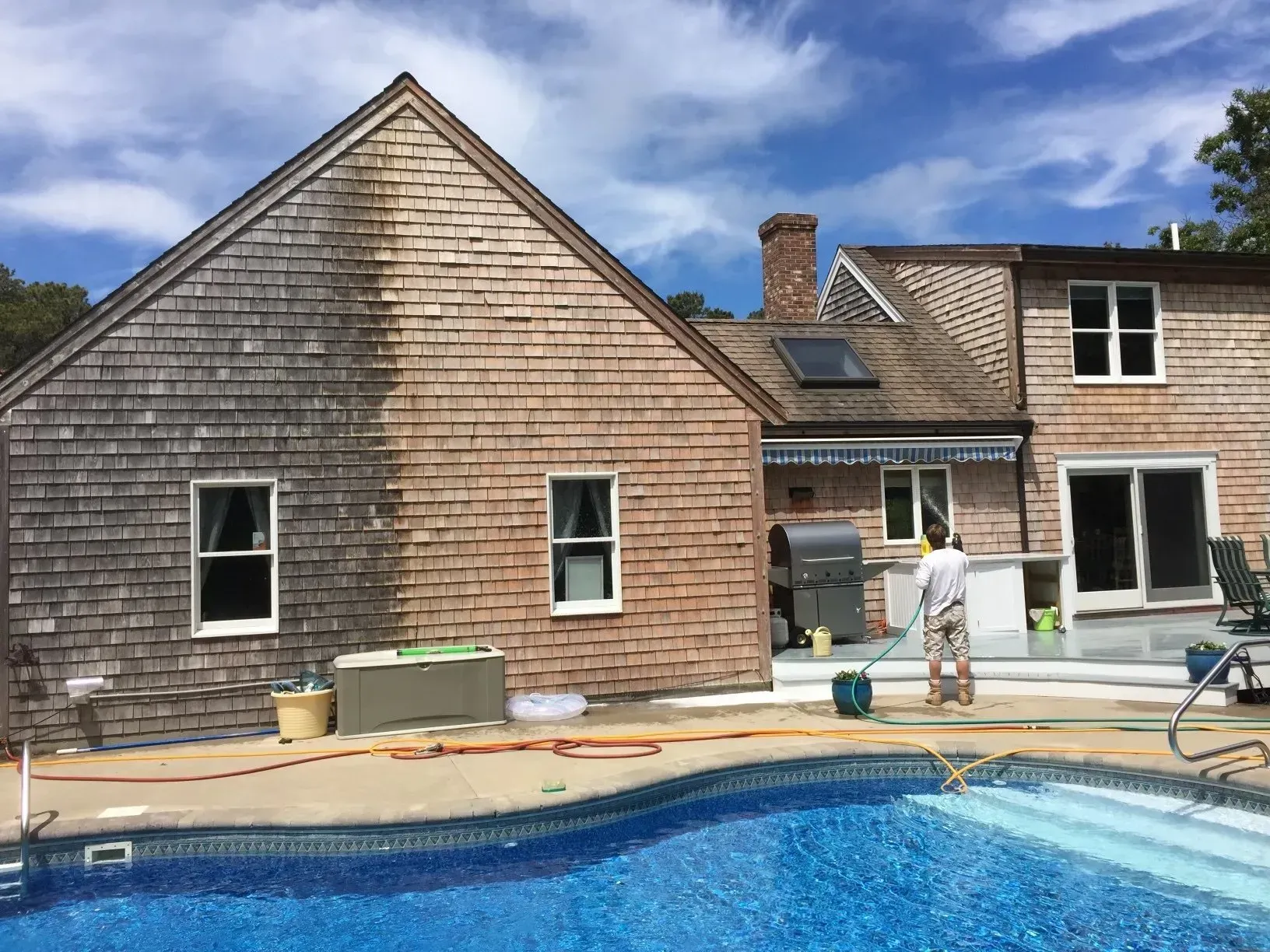 House being pressure washed, showing before and after effect on cedar shake siding, next to a pool.