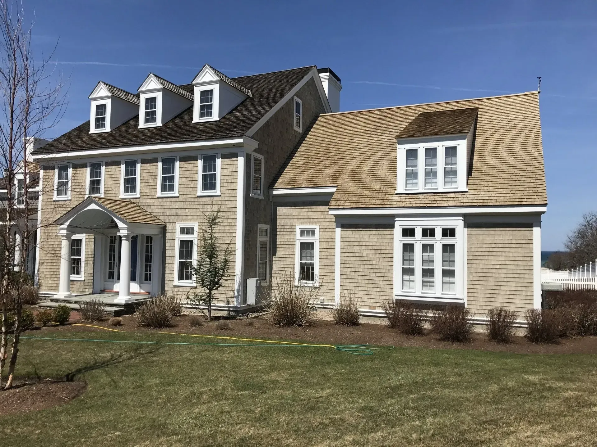 Two-story brick house with multiple dormers, white trim, and a small front yard on a sunny day.