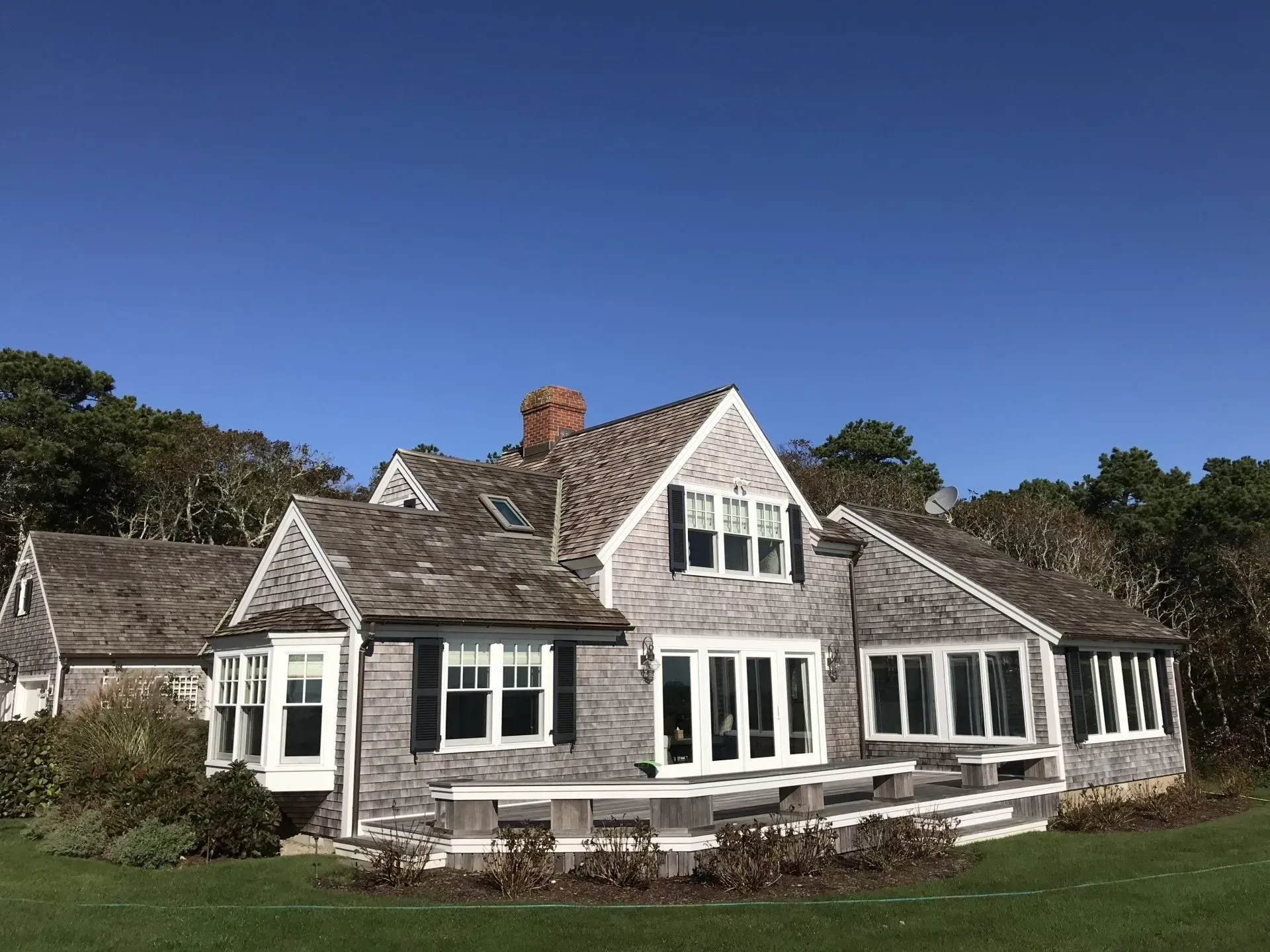 Gray shingled house with multiple gables and windows against a clear blue sky.