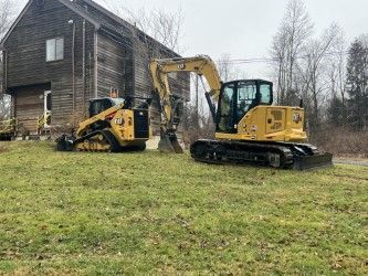 Two bulldozers are parked in a grassy field in front of a house.