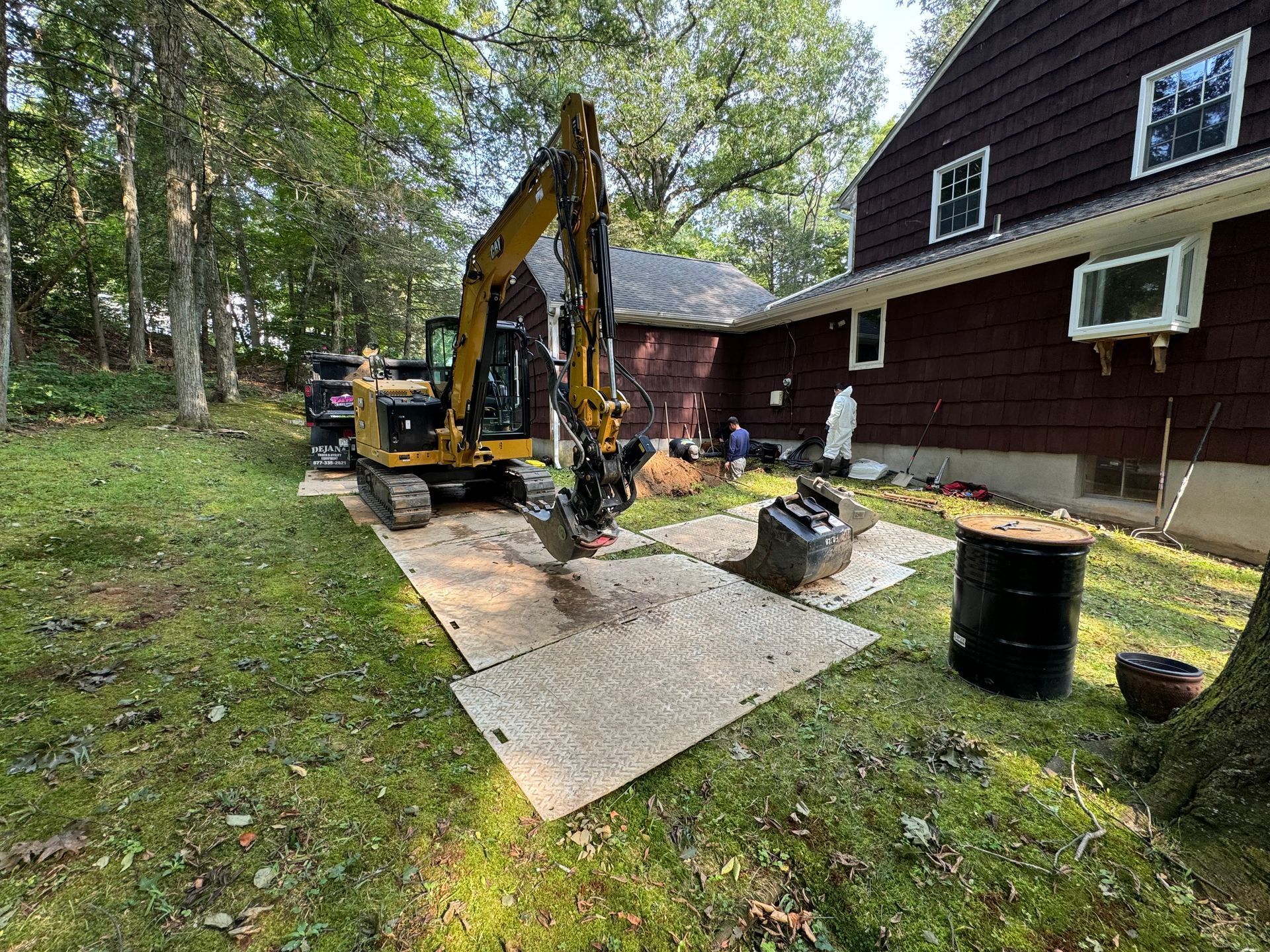 A yellow excavator is sitting on a wooden mat in front of a house.