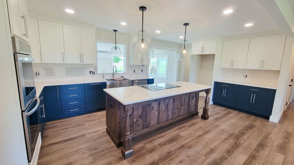 Spacious kitchen with blue and white cabinets, a wooden island with a cooktop, and hardwood floors.