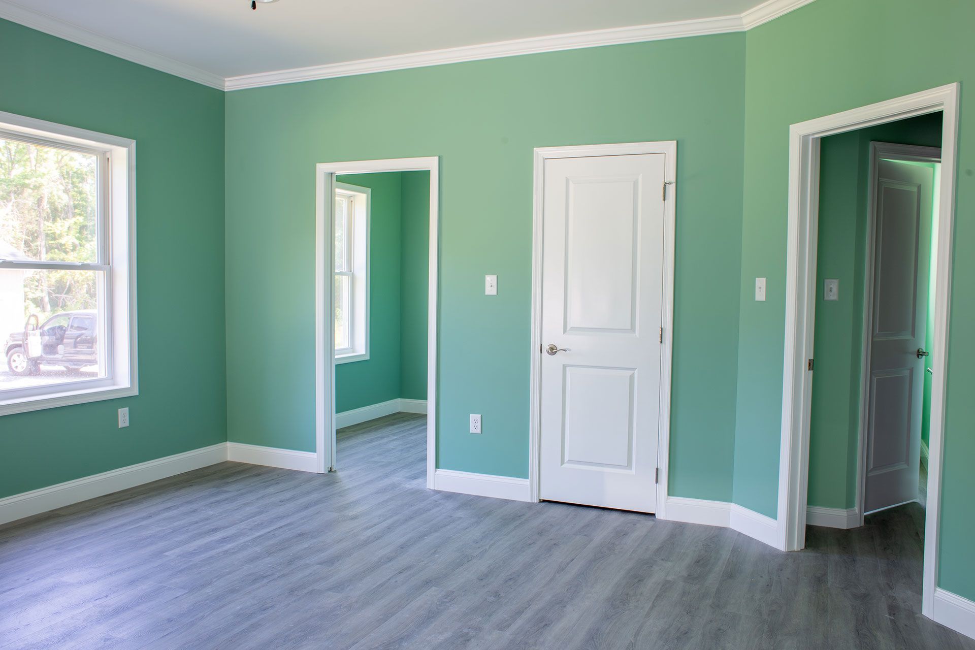 Empty room with seafoam green walls, white trim, doors, and gray wood-look flooring.