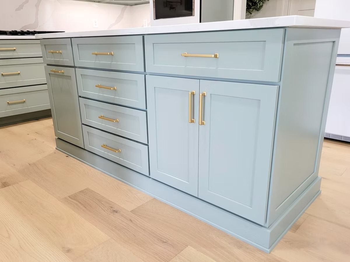 Light blue kitchen island with gold hardware and white countertop in a room with light wood floors.