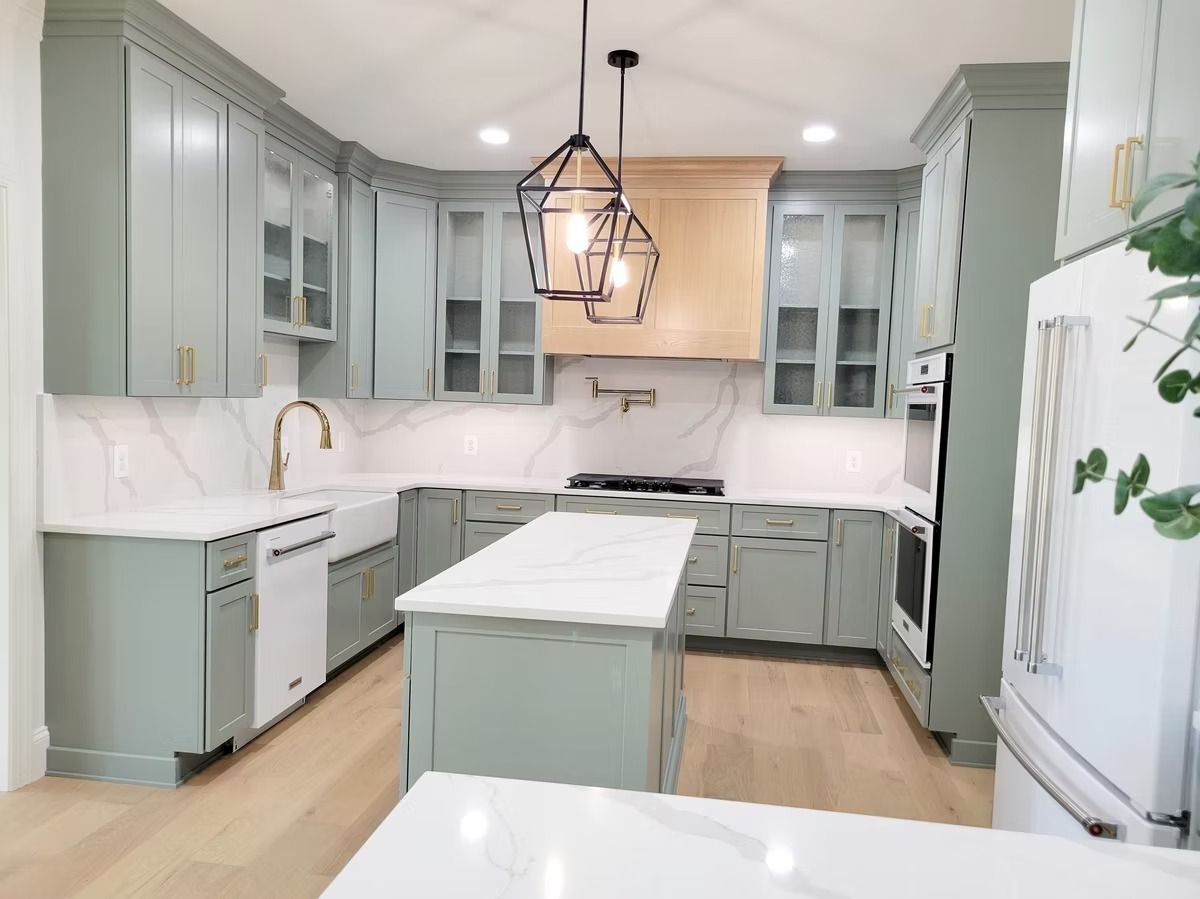 Green kitchen cabinets with white countertops, island, and light fixtures.