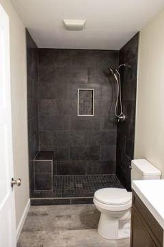 Dark tiled shower with built-in bench and recessed shelf, adjacent to a toilet and white countertop.