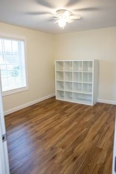 Empty room with wood floors, white shelving, and a window with blinds.