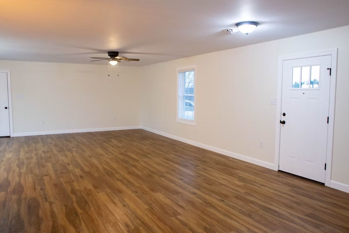 Empty living room with wood-look flooring, light walls, and a white front door.