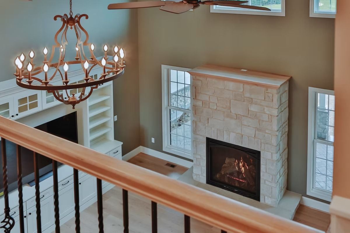View from a balcony of a living room with a fireplace, chandelier, and built-in shelving.