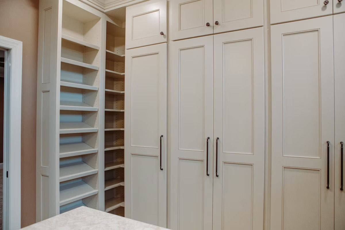 Built-in cream-colored closet with shelves and closed cabinet doors.