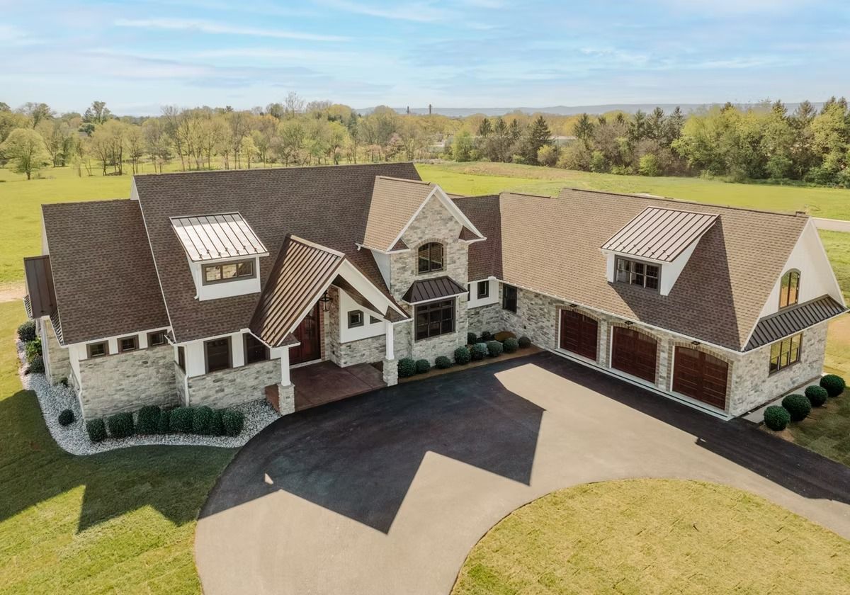 Sprawling stone-clad house with multiple rooflines, dormers, and a circular driveway on a grassy lot.