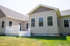 Beige house exterior with a deck, multiple windows, and a grassy yard.