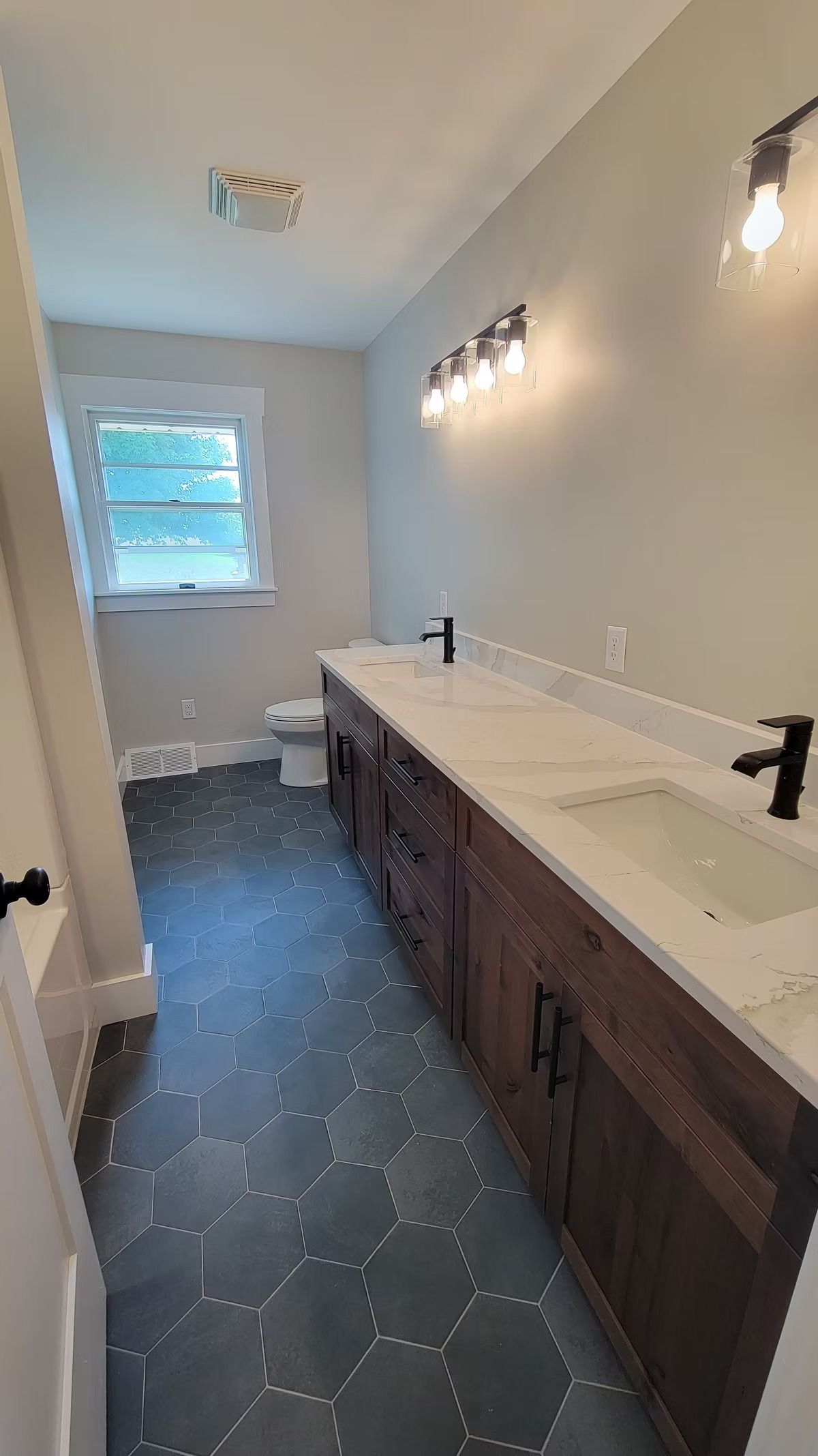 Bathroom with a long dark wood vanity, white countertop, and dark hexagon floor tiles.