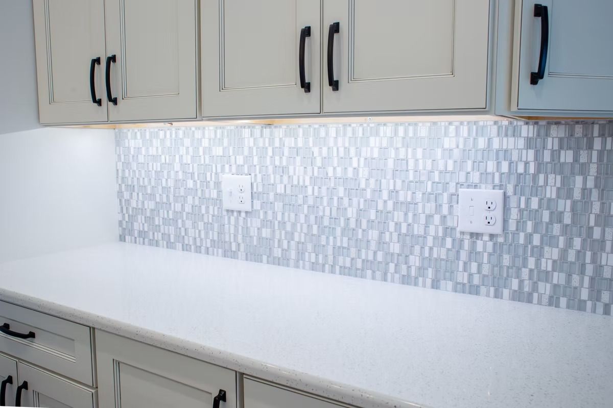 Kitchen counter with white cabinets, mosaic backsplash, and outlets.