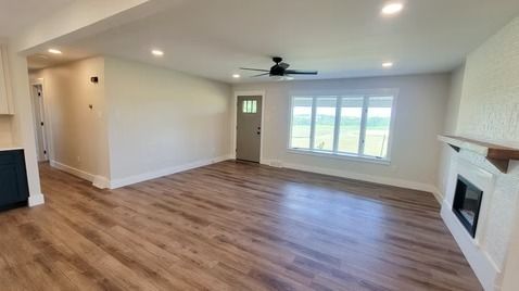 Empty living room with wood-look flooring, light walls, fireplace, and large window with exterior view.