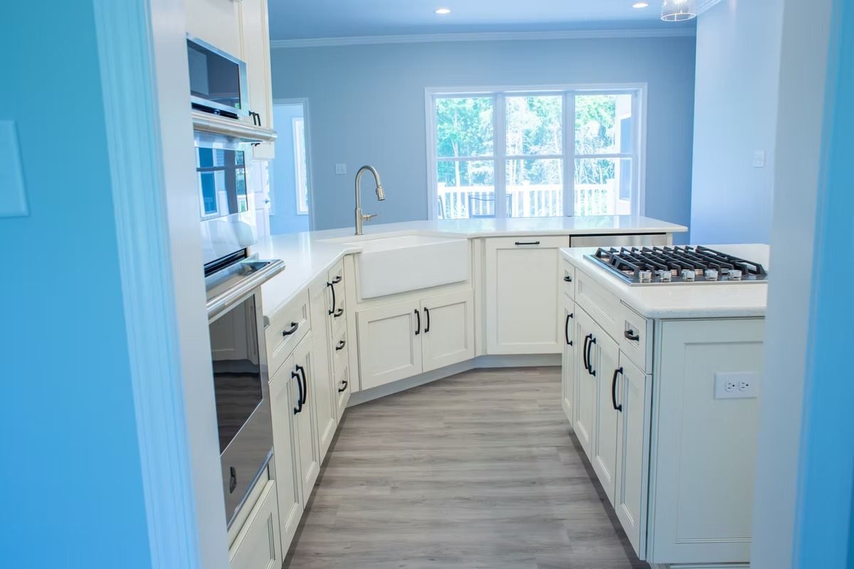Modern white kitchen with island, stainless steel appliances, and large windows.