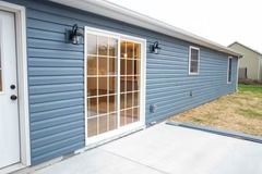 Blue-sided house with sliding glass door and concrete patio. Two wall lamps flank the door.