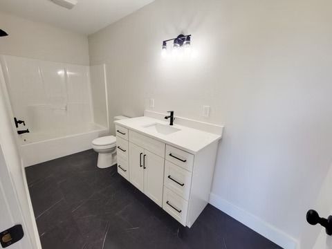Bathroom with white vanity, black faucet, and gray tile floor. White bathtub and toilet.