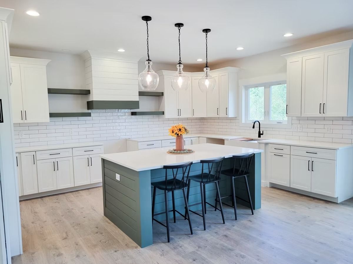 Modern white kitchen with teal island and three pendant lights; sunflower centerpiece.