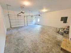 Empty garage with two doors, concrete floor, white walls, and two ceiling lights.