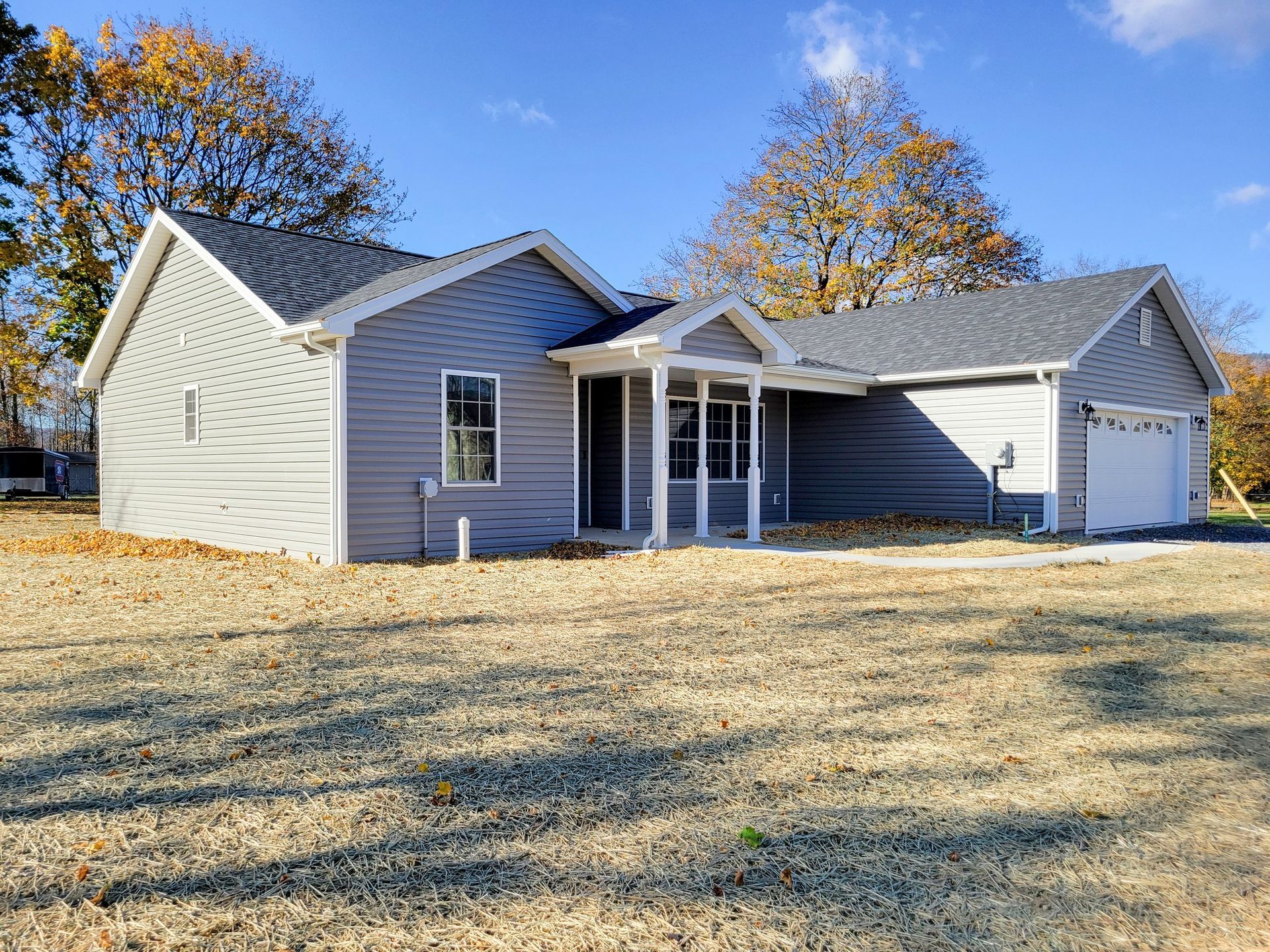 Gray house with white trim, porch, and garage on a brown grass field under a blue sky.