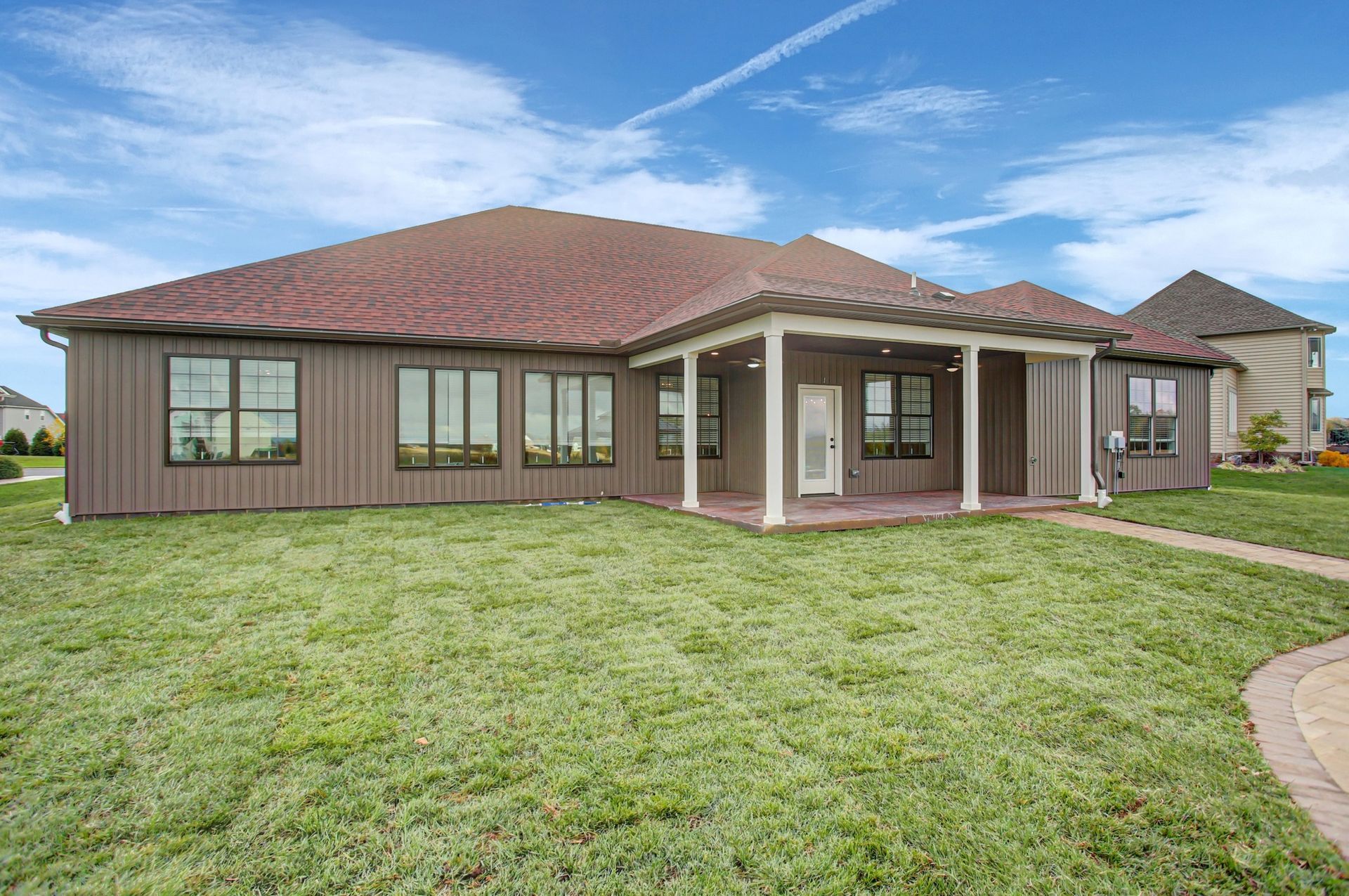 Brown house with covered porch, windows, and green lawn under a blue sky.