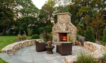 A stone fireplace is surrounded by chairs and a stone wall